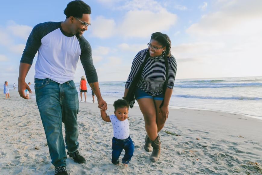 smiling parents holding curious baby by hand on the beach